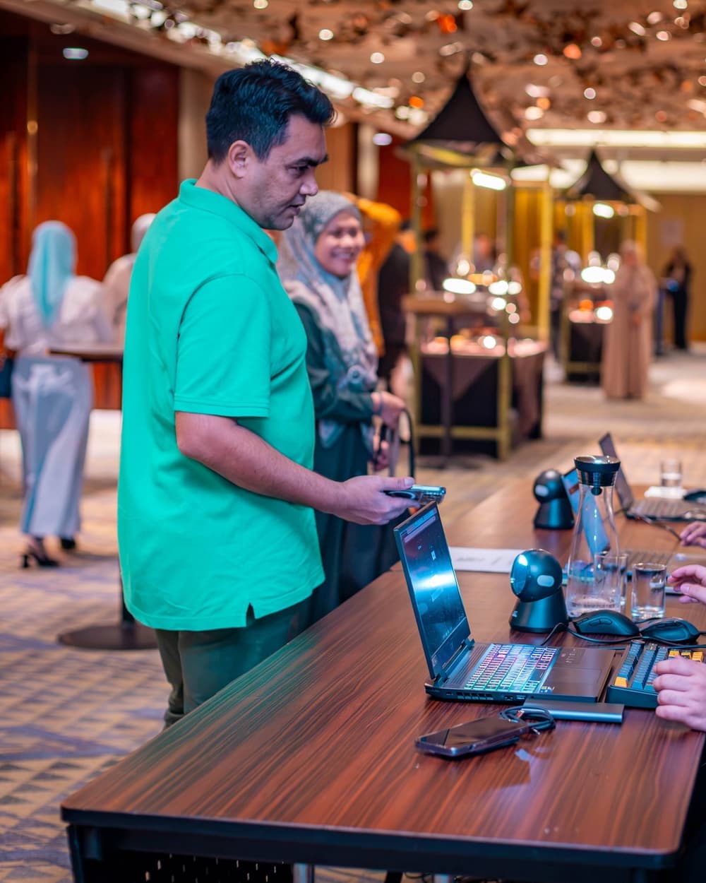 An attendee in a green shirt checking in at the registration desk as others queue behind him